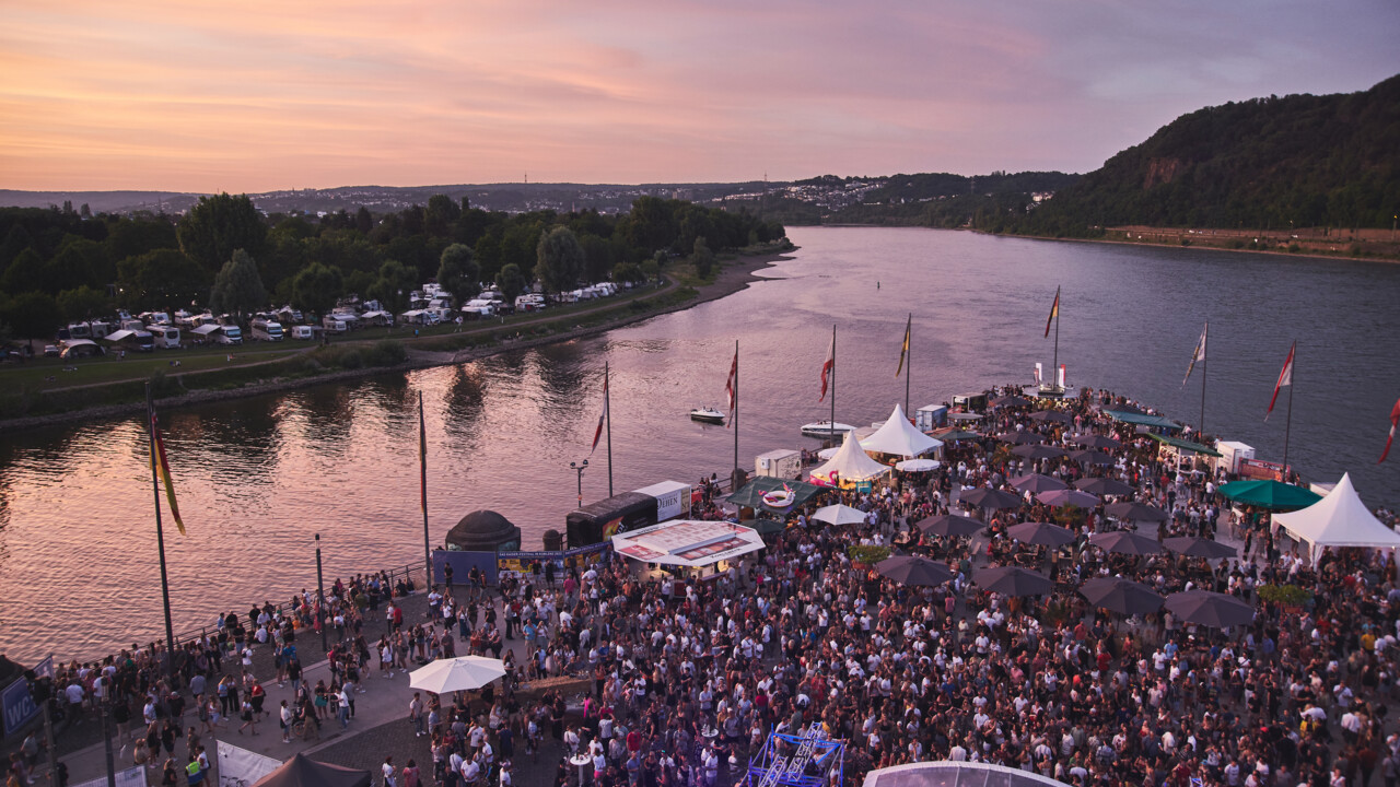 Electronic Wine © Picture Colada Blick von oben auf das Deutsche Eck bei Abenddämmerung während einer Veranstaltung, Menschengruppen stehen vor einer Bühne und an Ständen verteilt auf dem Gelände © Picture Colada